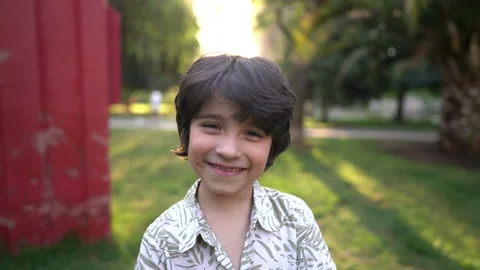 8 year old boy smiles at the camera in a park with a sunset behind his back Stock Footage
