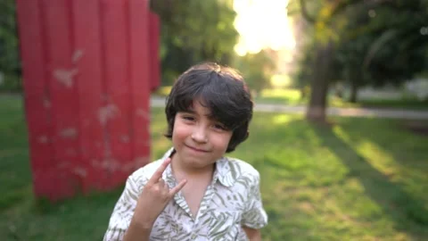 An 8-year-old boy smiling in a park poses making a symbol maloik Stock Footage 141989042