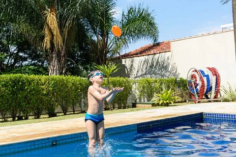 8 year old child with diving goggles jumping into the pool with a water bomb. Stock Photos