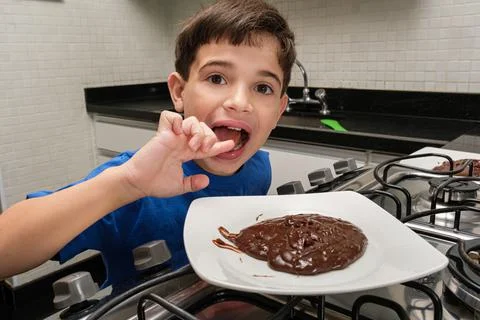 8 year old child in front of a plate of sweet brigadeiro and licking his fing Stock Photos