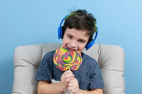 8 year old child with headphone and biting a big colorful lollipop. Stock Photos