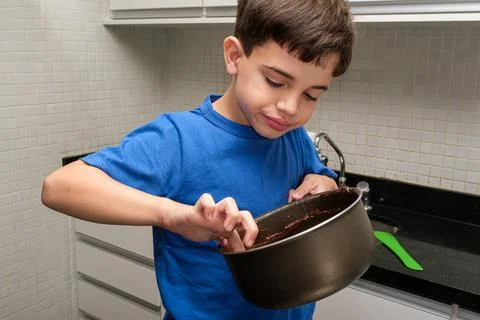 8 year old child in the kitchen picking up the brigadeiro in the pan with his Stock Photos