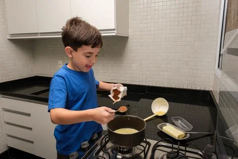 8 year old child putting a spoon of cocoa powder in condensed milk to make br Stock Photos