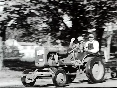 8mm Two men men driving tractor through town Video stock 153522653