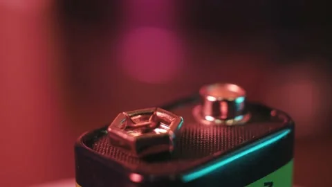 A 9-volt battery rotates and shines in rays of light on a colored background. Stock Footage 187039451