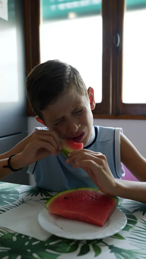 9 year old boy eating a slice of watermelon at home, vertical image Stock Footage 211044293