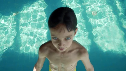 9 year old boy falling into the pool with blue water. Splashes fly in different Vidéo 106073724