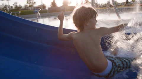 9 year old boy slides down waterslide and splashes into pool at splash pad Stock-Footage 233946973