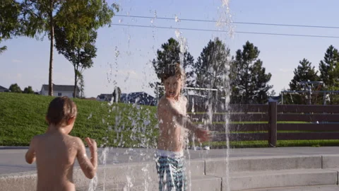 9 year old boy spins inside splash pad water jets as 6 year old boy runs around Видео 233938864