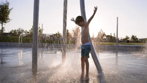 9 year old boy stands under splash pad water raining down with arms open Stock Footage 233947273