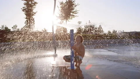 9 year old boy under giant splash pad water sprinkler, observing how it works Stock-Footage 233945450