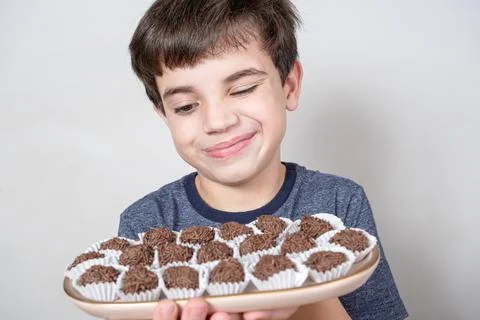 9 year old looking at a tray with several Brazilian fudge balls and with one  Stock Photos