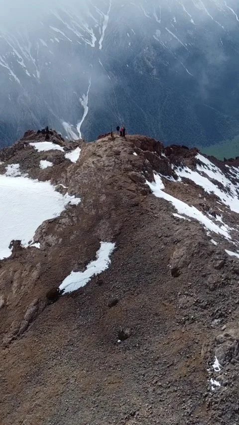 9:16: Drone Aerial: Tiny Climbers on Snow-Covered Mountain Peak Above Clouds Video stock 331593010