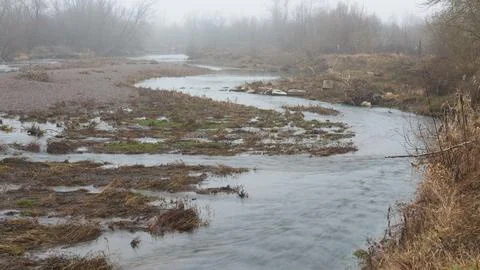 9Winding river flows beneath high riverbank during foggy day. Stock Photos