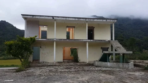 Abandoned broken down house with concert courtyard surrounded by green hills Stockbeeldmateriaal 80706295