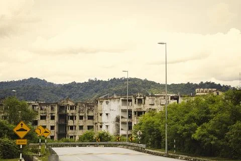 An abandoned building is surrounded by greenery under a cloudy sky. Stock Photos
