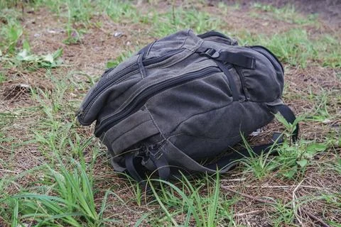 Abandoned dark canvas backpack resting on the dry forest floor terrain Stock Photos