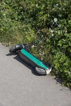 Abandoned e-scooter lying in grass by sidewalk Stock Photos