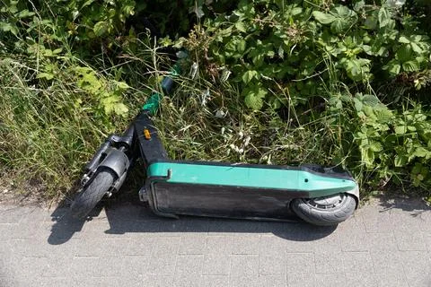 Abandoned e-scooter lying in grass by sidewalk Stock Photos