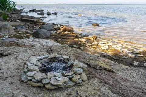 Abandoned fire ring on Baltic Sea beach beside rocky coastline Stockfoto's
