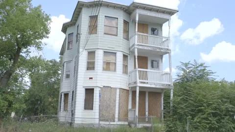 Abandoned house, boarded up windows, trees, chain link fence, cars passing 库存影片 304367478