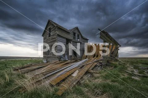 Abandoned house on the prairies with storm clouds overhead at sunset Stock Photos