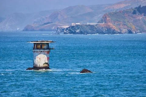 Abandoned lighthouse structure in middle of bay with distant mountainous coast Stockfoto's
