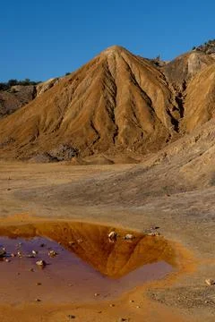 Abandoned mining grounds with eroded hillsides and reflections in a dirty pool 스톡 사진