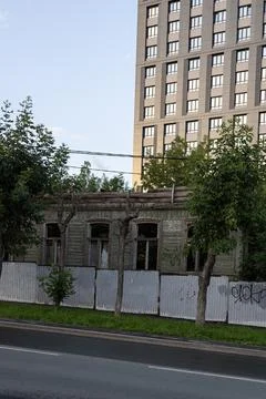 Abandoned old building with broken windows. Fence and trees along the road. Stock Photos
