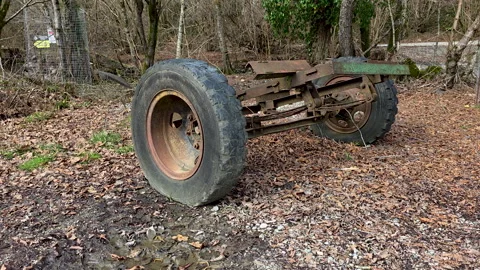 Abandoned rusty axle with a flat tire resting on a muddy forest floor covered in Vídeo Stock 329614282