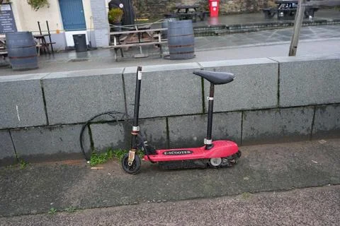 Abandoned Rusty Red E-scooter Leaning On Wall In Conwy, North Wales Stock Photos