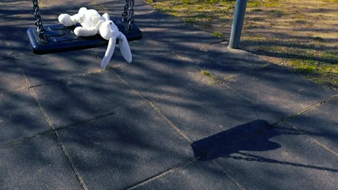 Abandoned Stuffed Bunny Swinging on an Empty Playground Swing Stock Footage 334351322