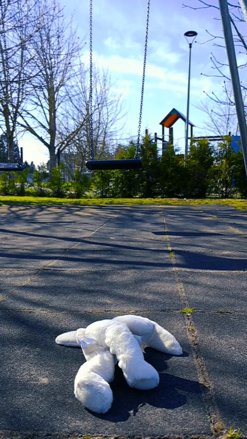 Abandoned Stuffed Bunny Toy Lying Under a Swing at an Empty Playground Stock Footage 334090698