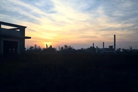 Abandoned warehouse in a field with an industrial complex in the distance at  Stock Photos