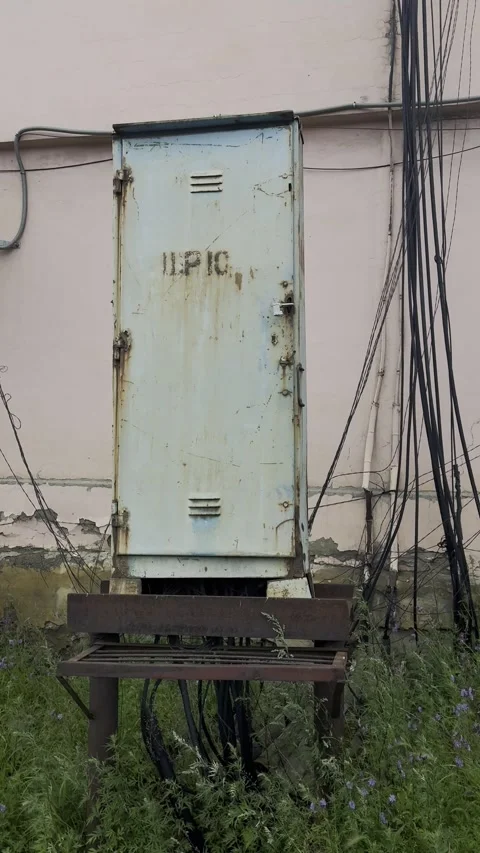 Abandoned weathered electrical utility box with rusted metal frame, tangled powe Stock Footage 339995781