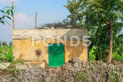 Abandoned yellow rocked hut with single green wooden door, tropical green trees Stock Photos