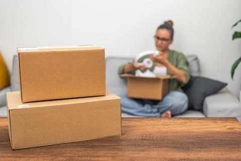 Able with blank mock-up parcel boxes, woman in background unboxing an online Stock Photos