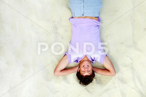 Above angle of handsome teenager lying on sand and laughing Stock Photos