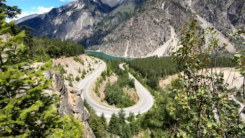 Above a bend in road surrounded by mountains and cars driving on road trip Stockbeeldmateriaal 100418455