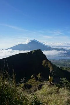 Above Cloud Nine, Mount Batur's Peak, Asian Man Trekker under Azure Sky and.. Stock Photos