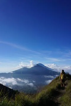 Above Cloud Nine, Mount Batur's Peak, Asian Man Trekker under Azure Sky and.. Stock Photos