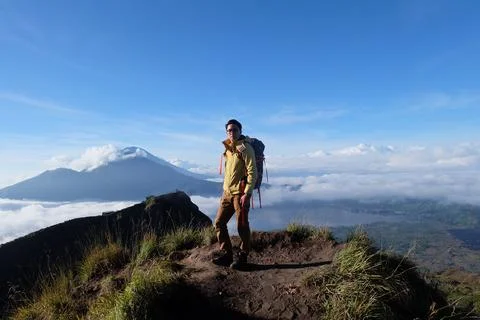 Above Cloud Nine, Mount Batur's Peak, Asian Man Trekker under Azure Sky and.. Stock Photos