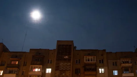 Above a multi-storey building, the moon moves in the night sky in clouds, Stock Footage 143586759