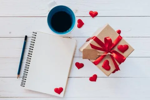 Above notebook, coffee cup, gift box, red ribbon, tag and pencil on white w.. Stock Photos
