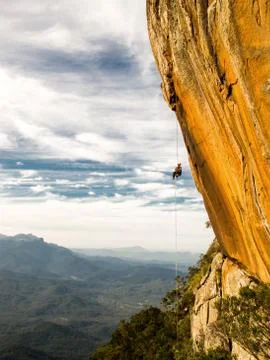 Abseiling a negative yellow rock wall with mountains on background Stock Photos