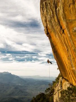 Abseiling a negative yellow rock wall with mountains on background Stock Photos