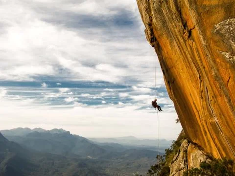 Abseiling a negative yellow rock wall with mountains on background Stock Photos