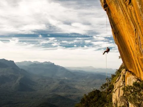 Abseiling a negative yellow rock wall with mountains on background Stock Photos
