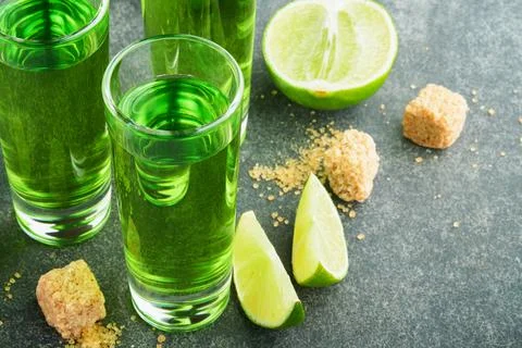 Absinthe. Two glasses of absinthe with cane sugar and lime on dark background Stock Photos