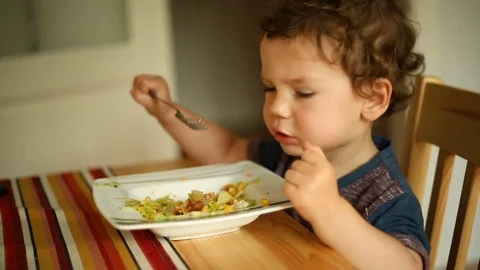 Absorbed little boy sitting at the table and eating delicious lunch Stock Footage 76183394